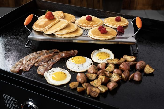The stainless steel warming rack holds a stack of pancakes topped with strawberries, surrounded by other breakfast items.