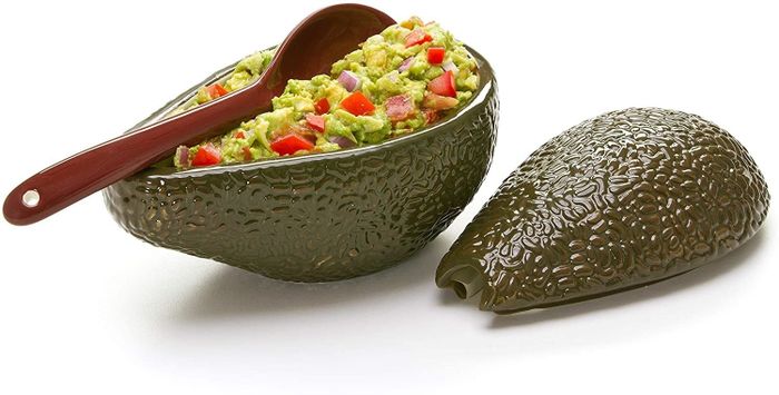 An avocado-shaped bowl opened to reveal a serving of guacamole, complete with a matching spoon.