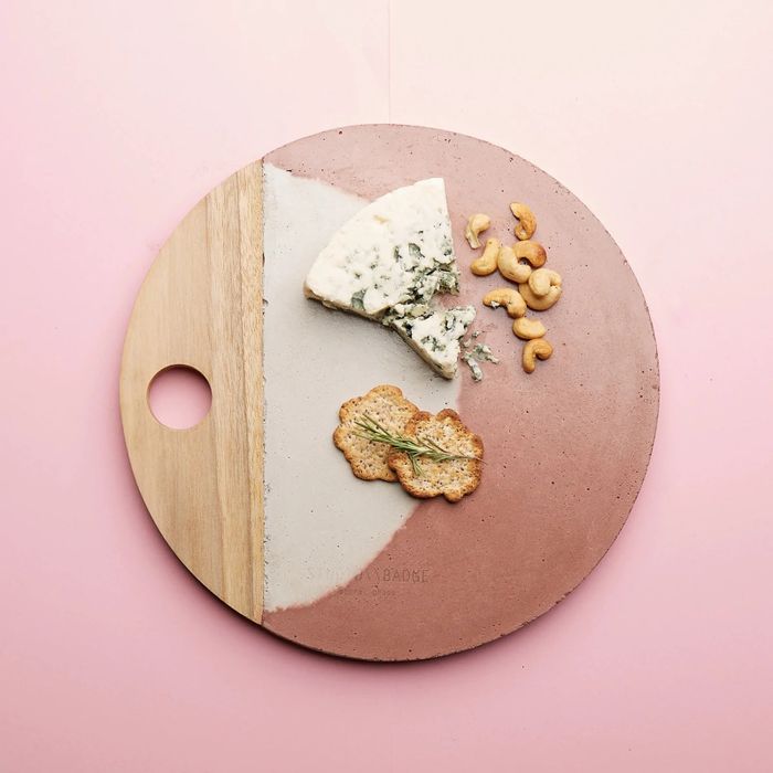 A round cheese board featuring a wooden handle with light gray and burnt orange dyed concrete accents, perfect for any gathering.
