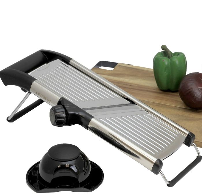 A silver and black device sits beside a tan cutting board with an assortment of vegetables placed on it.