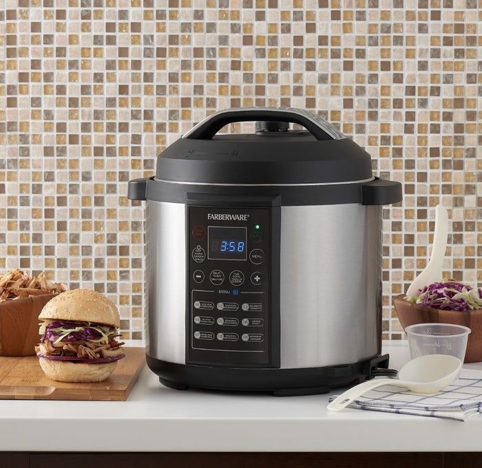 The black and silver pressure cooker sits on a countertop, surrounded by pulled pork and coleslaw.
