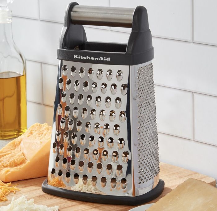 The stainless steel grater bears the 'KitchenAid' name and comes with a black handle.