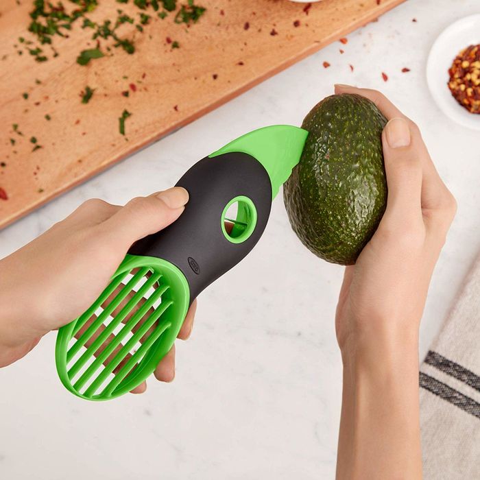 A hand using an avocado tool to slice open a perfectly ripe avocado.
