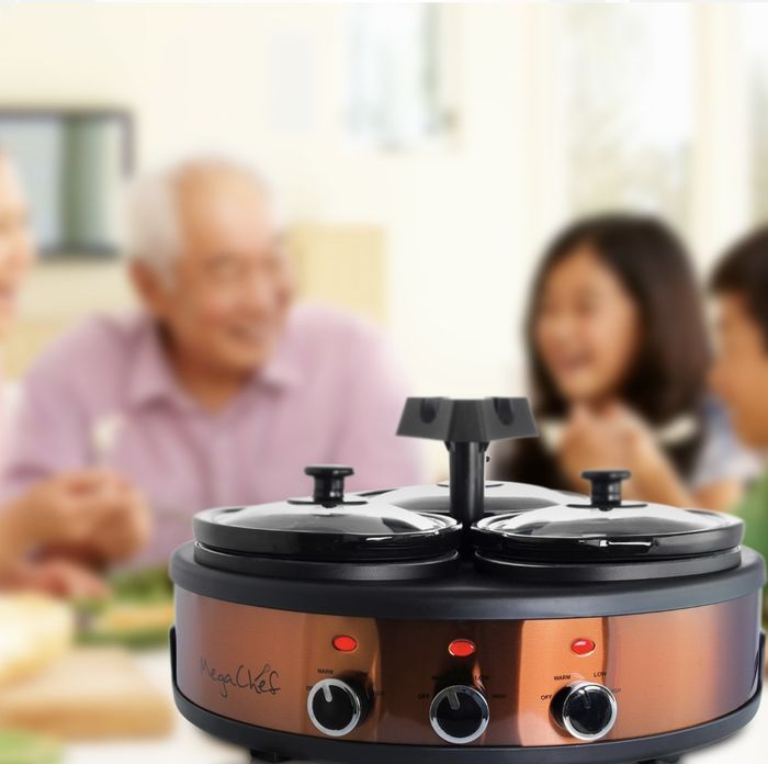 The slow cooker features a stylish copper and black design, with a cheerful group of young and old people laughing in the background.
