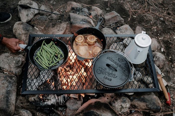 The cast iron set sits over an outdoor fire, roasting various foods to perfection.