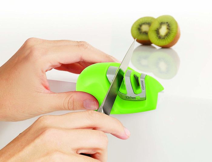 Gliding a knife through a slit in a green knife sharpener for precision and ease.