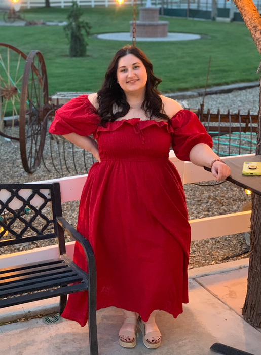 A reviewer in a red dress with off-shoulder sleeves, exuding a chic and daring vibe.