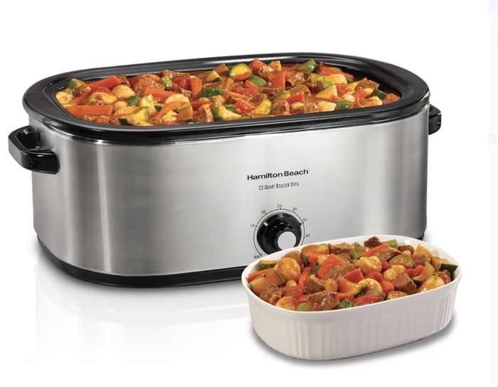 The roaster oven is filled with vegetables and meat, accompanied by a nearby white dish with the same ingredients.