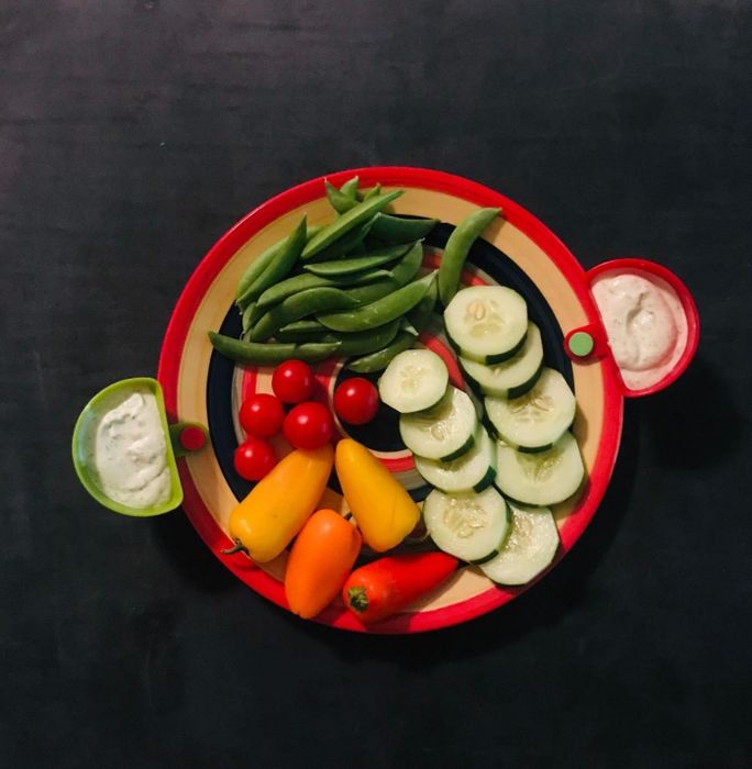 Two dip clips attached to a plate filled with fresh vegetables, making dips easy to enjoy.