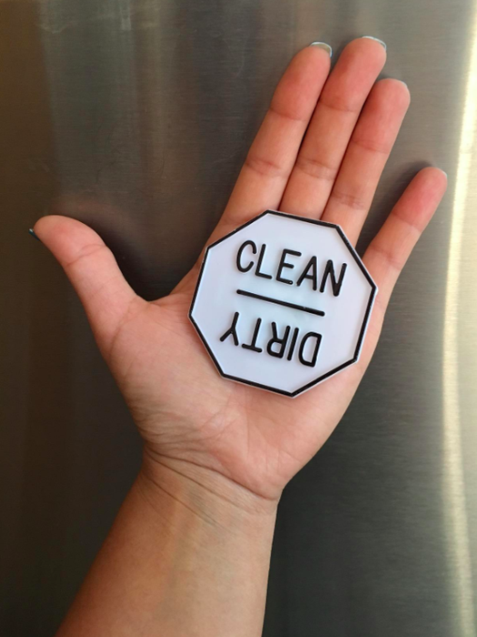 A hand holding a magnet that says 'clean' on the top and 'dirty' on the bottom, ready for the dishwasher.