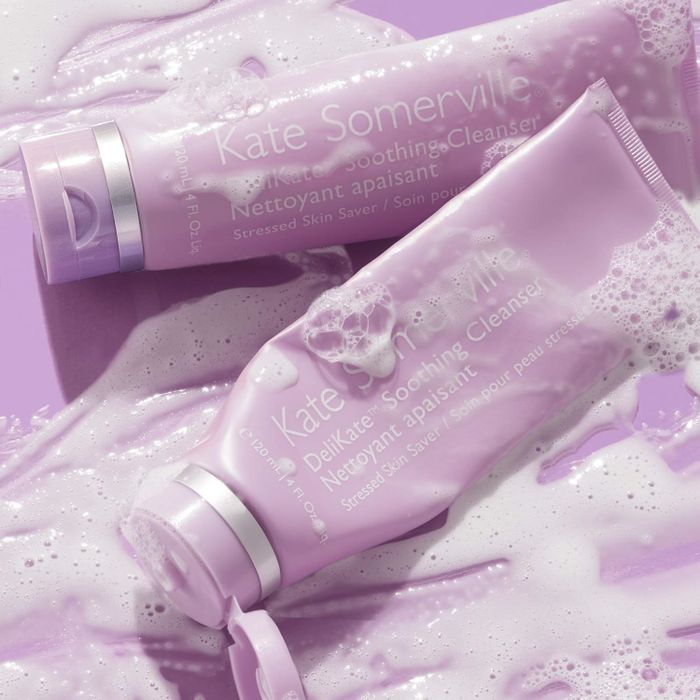 Two tubes of Kate Somerville Delikate Soothing Cleanser are immersed in a bed of foamy bubbles, creating a visually appealing display.