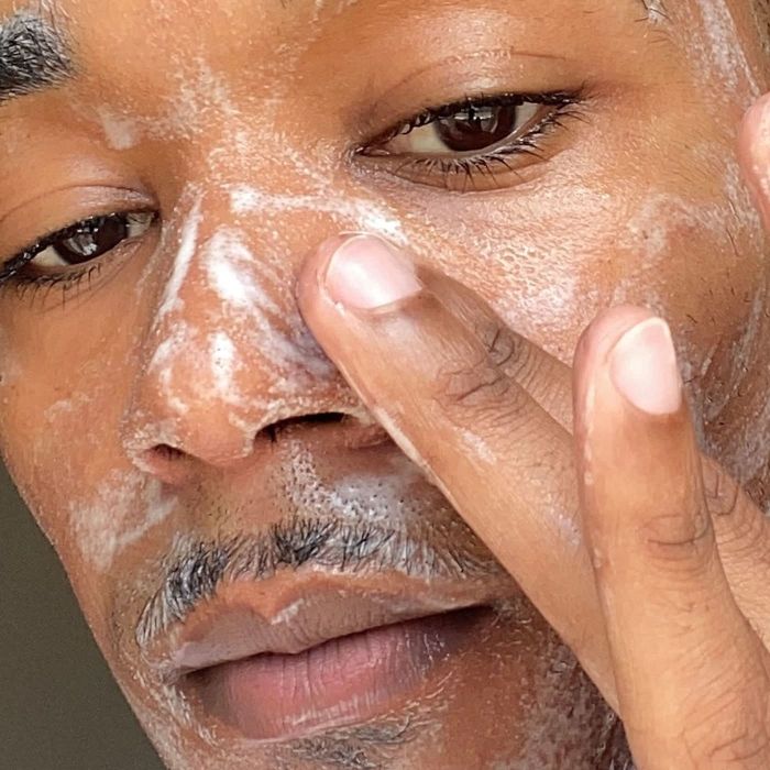 A close-up shot captures a person applying face cleanser, highlighting their smooth skin and the gentle motion of their fingers during the cleansing process. Only their face and fingers are visible.