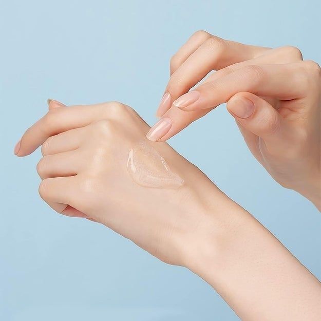 A close-up shot shows a person’s hand applying a clear gel or cream to the back of their other hand.