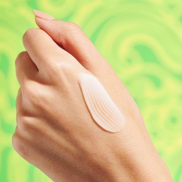 A close-up image shows a hand with a swatch of skin cream, set against a vibrant green background.