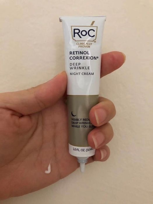 A person holds a tube of RoC Retinol Correxion Deep Wrinkle Night Cream, with a dab of the cream on their fingertip.