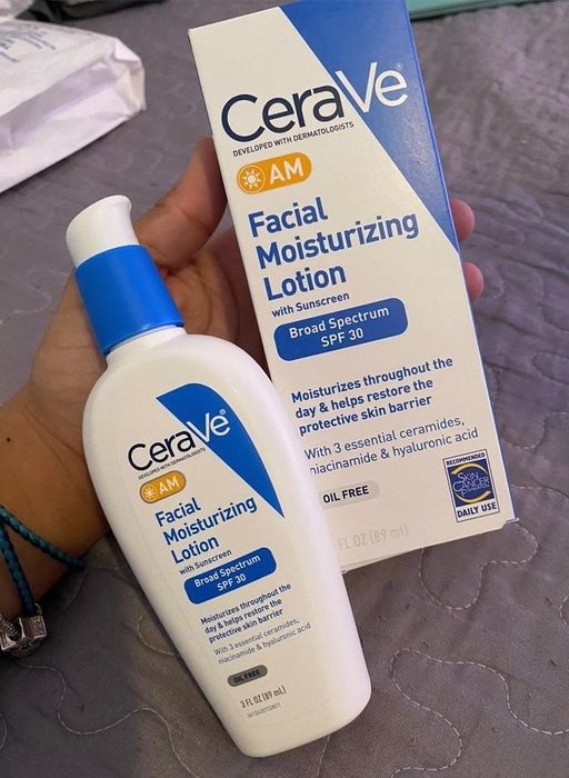 A hand holds CeraVe AM Facial Moisturizing Lotion with SPF 30. The box highlights its ability to moisturize and restore the skin's protective barrier.