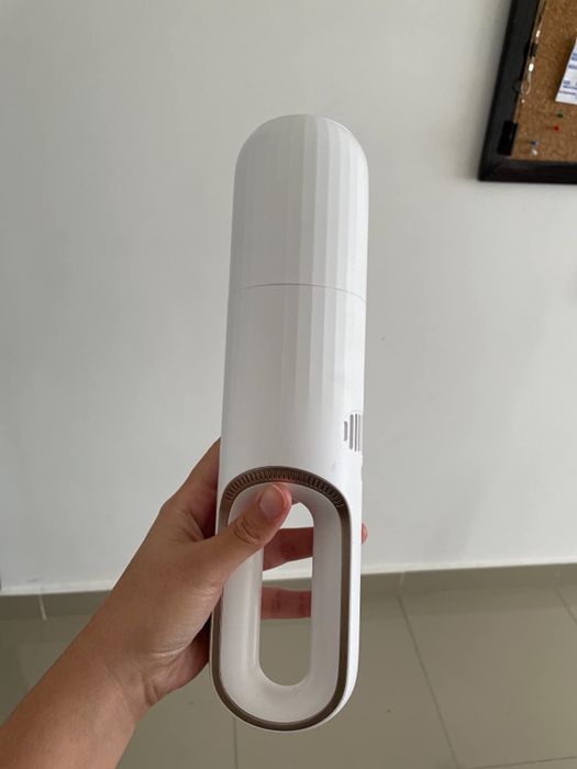 A reviewer holding the small white portable vacuum, ready for use.