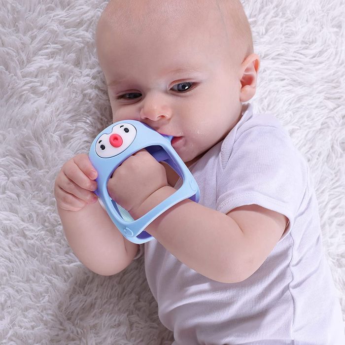 A baby gently holding a blue pacifier in their hand, happily sucking on it.