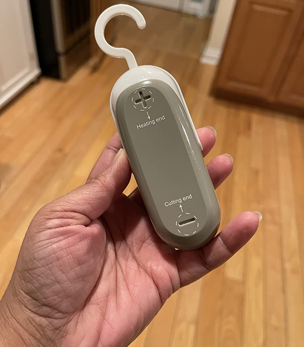 A reviewer is seen holding the small grey bag sealer, which has a hook on the top for easy handling.