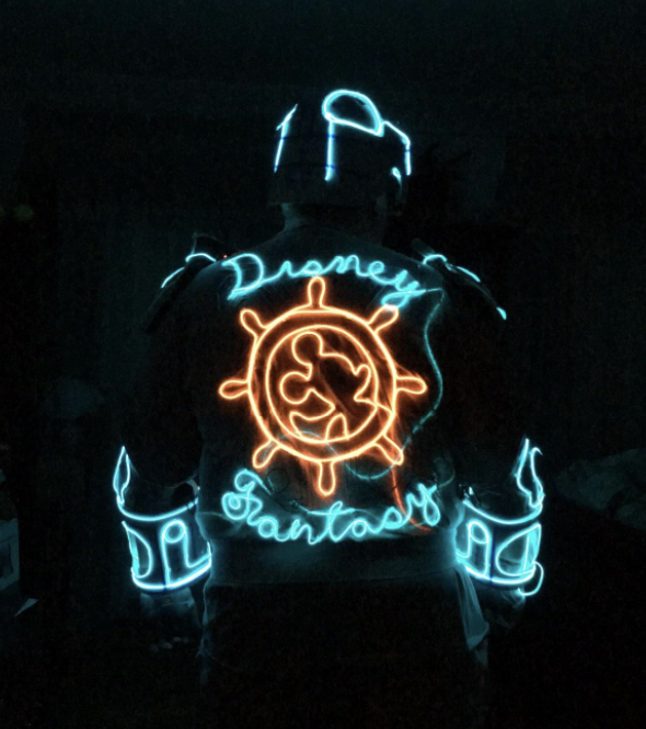 An individual adorned in neon lights, wearing a jacket with a Disney-inspired pattern.