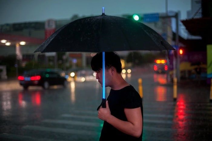 A person holding the umbrella, which features a glowing shaft resembling a lightsaber.