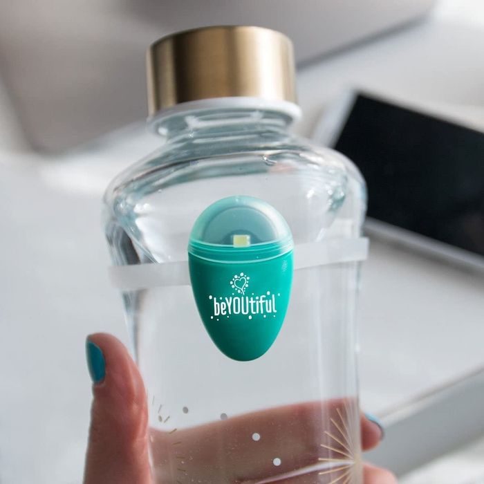 A tear-drop shaped hydration tracker attached to a silicone band, which is then connected to a glass water bottle, making it easy to keep track of hydration.