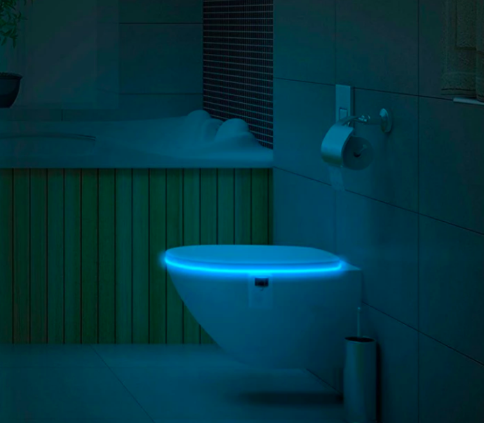 Closed toilet seat illuminated from within in a dimly lit bathroom
