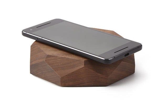 A smartphone placed on a geometric walnut wood charger with a flat surface.