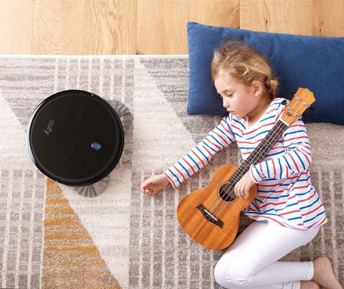 A child peacefully sleeping on the floor while the robot vacuum does its job nearby.