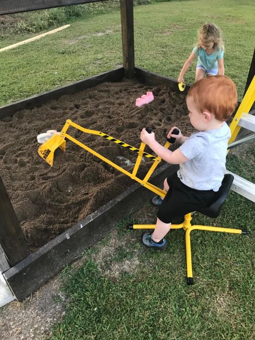 A child is seen sitting on the excavator, happily scooping sand in the sandpit.