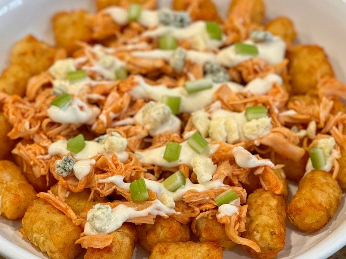 A plate of loaded tater tots with shredded chicken, cheese, green onions, and sauce. Perfect for sharing at casual gatherings or parties