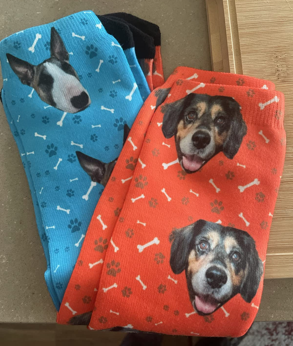 Two pairs of socks with dog faces and bone patterns, one pair in blue and the other in red, displayed on a wooden surface