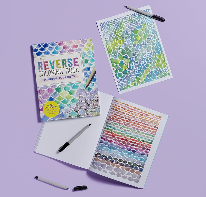 A reverse coloring book with open pages showcasing abstract patterns; pens scattered around