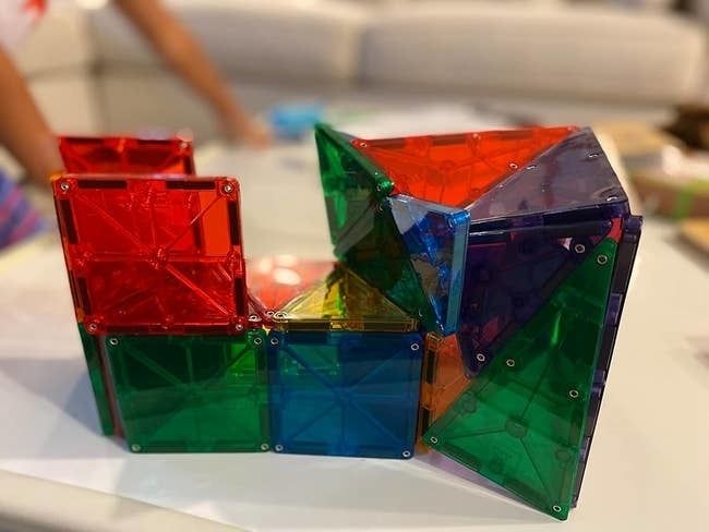 A colorful structure made from translucent magnetic tiles, displayed on a table as a fun, creative building toy for children