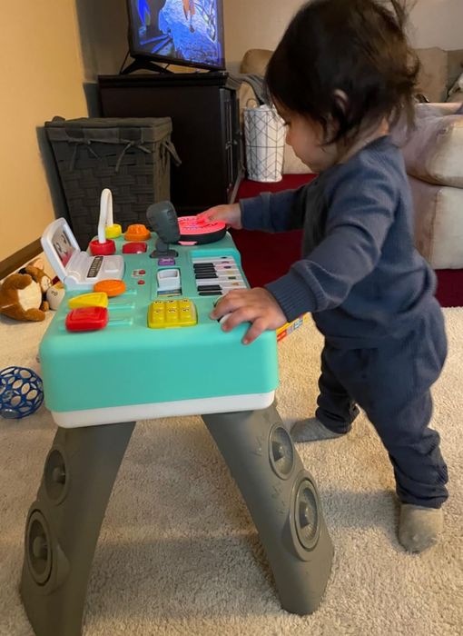 A toddler standing in front of a DJ kids turntable set, ready to mix some tunes.