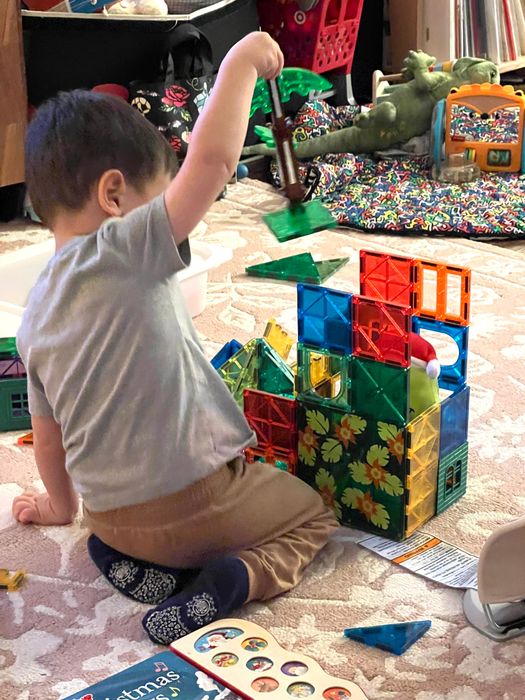 A child assembling colorful magnetic building blocks on a rug, surrounded by other toys and a book