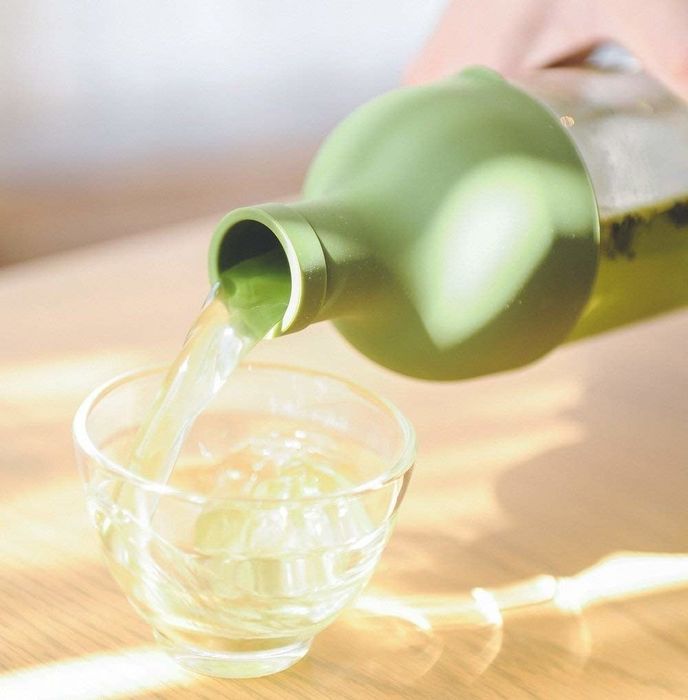 A hand gently pouring green tea from the bottle.