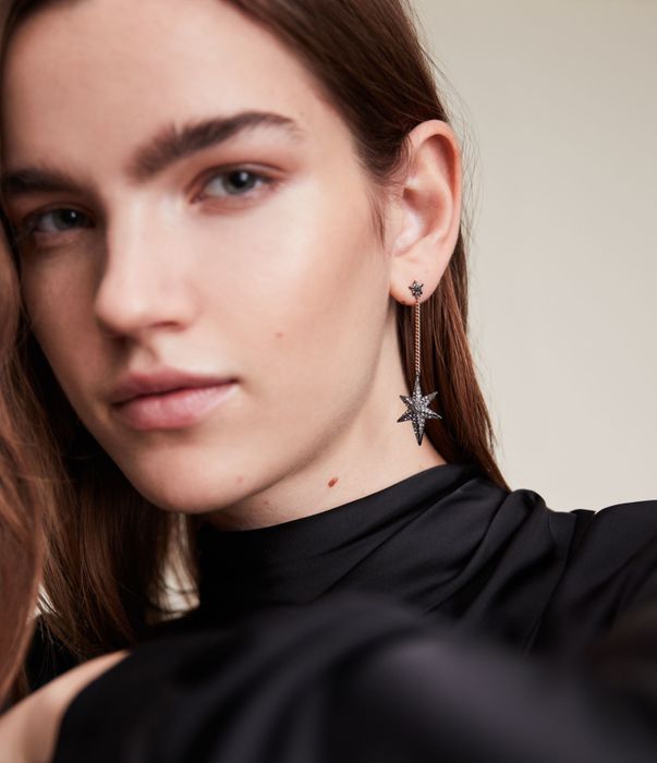 A model wearing hematite and gold-tone earrings, featuring a star on the lobe and a larger star dangling from a chain.