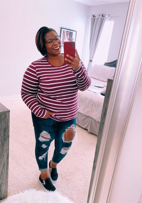 A reviewer dressed in a red and white tee paired with jeans and slide-on sneakers