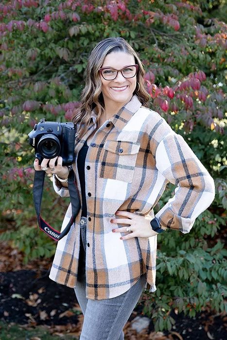 A reviewer sporting a brown and blue shacket, paired with a camera and light-wash jeans