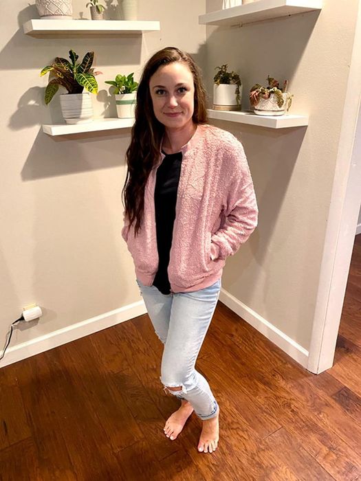 A reviewer sporting a black top, a pink jacket, and light wash denim