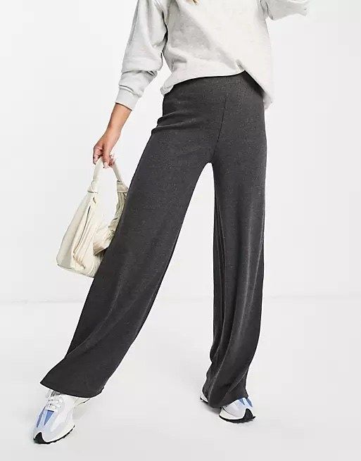 A model styled in grey pants, a white top, blue-and-white shoes, and a white bag