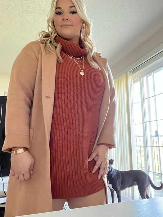 A reviewer styled in an orange dress paired with a tan coat