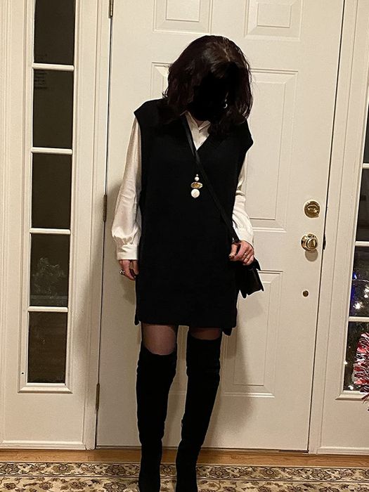 A reviewer styled in a black oversized sweater dress layered over a white shirt and black shoes