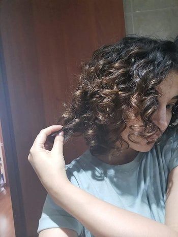 A reviewer pulls on a curly ringlet to highlight the texture.