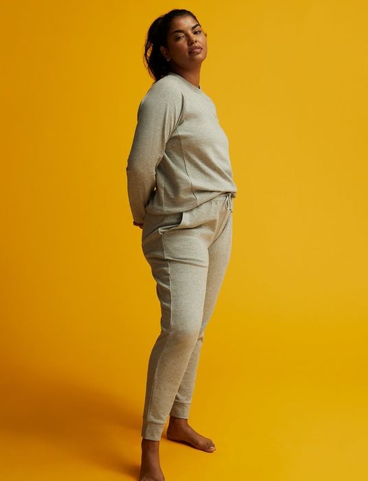 The model is wearing light gray joggers paired with a matching sweatshirt.