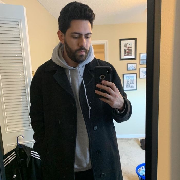 A reviewer is seen sporting a gray sweatshirt underneath a stylish peacoat.
