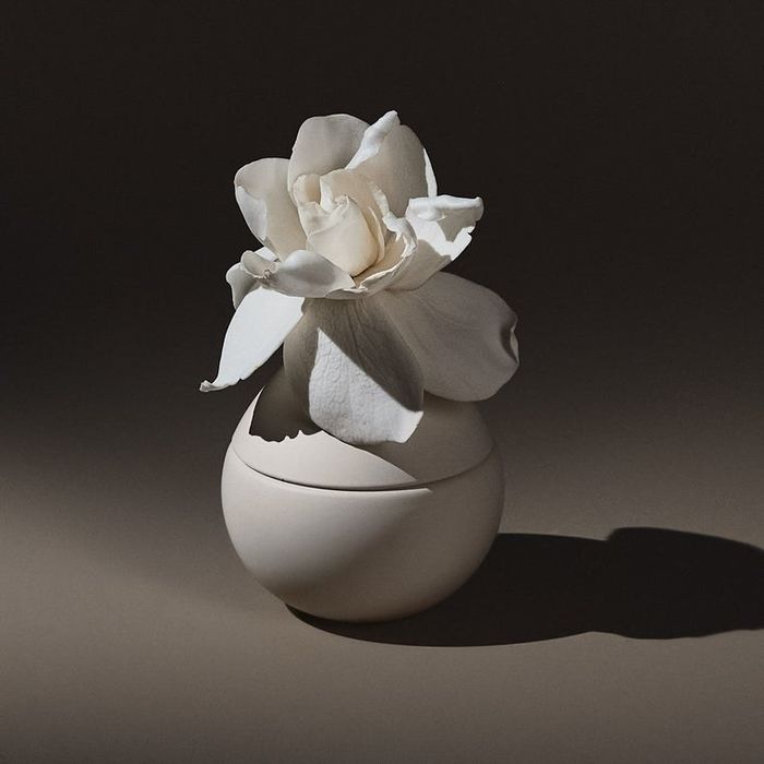 A creamy white perfume bottle with a delicate white rose atop it.