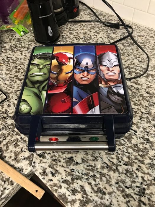 A reviewer showcasing the square waffle iron, with images of Hulk, Iron Man, Captain America, and Thor on the top.