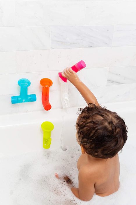 A child pouring water through one of the bath pipes attached to the wall during playtime.
